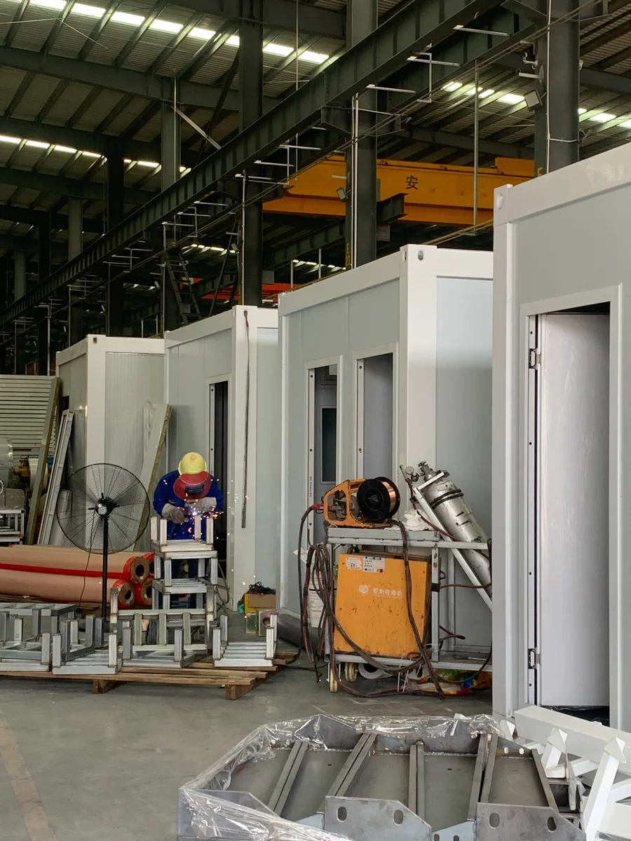 A worker welding components beside modular building units